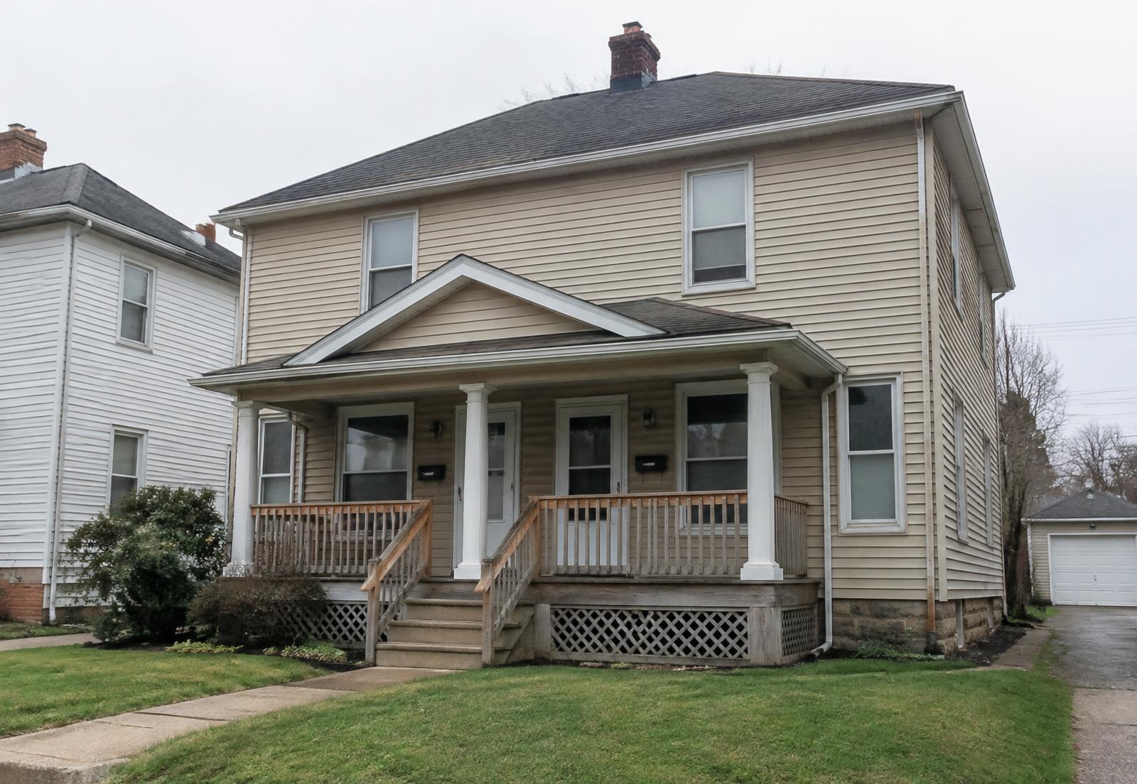 Illustrative photo: an older two-family wood-frame house with vinyl siding and a front porch